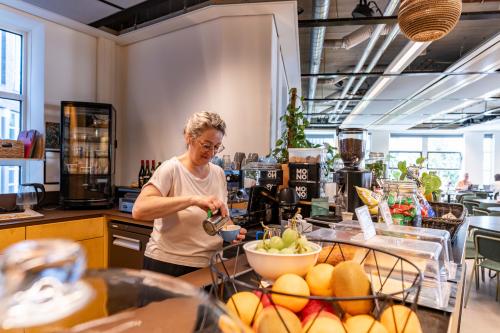 Binnenzicht van kantoorruimte op Fluwelen Burgwal 58, Den Haag Centrum, met een persoon die koffie zet bij een pantry, omringd door fruit en planten.