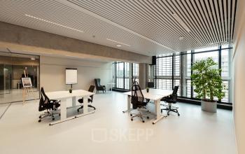Moderne kantoorruimte te huur op Waldopstraat 5, Den Haag Centrum. Lichte werkruimte met grote ramen, twee bureaus met stoelen en een flipover, ideaal voor creatieve werkprocessen.