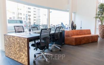 Moderne kantoorpand op Kalvermarkt 53, Den Haag Centrum, met werkbanken, bureaustoelen en een bruine zitbank. Grote ramen geven veel natuurlijk licht.