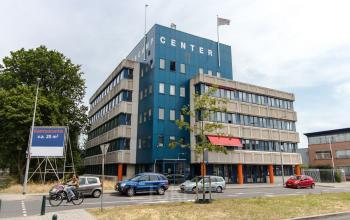 Buitenzicht op kantoorpand met meerdere verdiepingen op Platinaweg 25 in Den Haag Escamp, ideaal voor kantoorruimte huren. Diverse auto's geparkeerd voor het gebouw, groene omgeving.