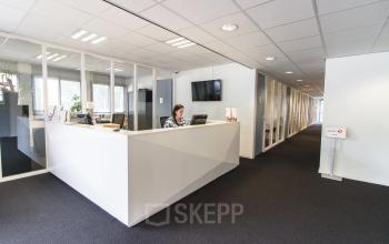 Moderne kantoorruimte in Den Haag Escamp met receptiebalie en glazen wanden. Een persoon helpt een klant. Ideaal voor bedrijven die kantoorruimte willen huren in een professioneel kantoorpand.
