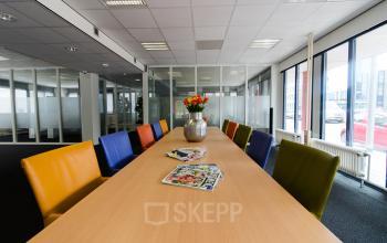 Moderne kantoorruimte huren aan de Platinaweg 25, Den Haag Escamp, met kleurrijke stoelen rondom een vergadertafel, ideaal voor zakelijke bijeenkomsten in een lichte, luchtige omgeving.