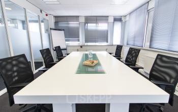 Kantoorruimte huren in Den Haag, Escamp: Moderne vergaderruimte op Platinaweg 25, met glazen tafel, rolstoelen en natuurlijk licht door grote ramen.
