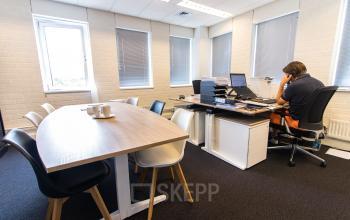 Kantoorruimte te huur aan de Platinaweg 25 in Den Haag Escamp, met een kantoor en vergadertafel. Een persoon voert zakelijke activiteiten uit aan een bureau.