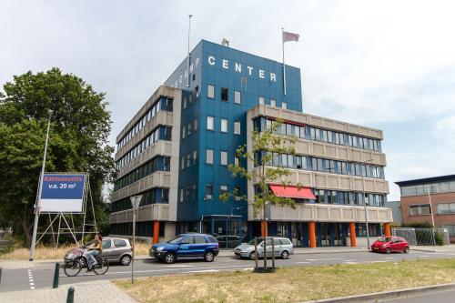 Buitenzicht op kantoorpand met meerdere verdiepingen op Platinaweg 25 in Den Haag Escamp, ideaal voor kantoorruimte huren. Diverse auto's geparkeerd voor het gebouw, groene omgeving.