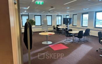 Kantoorruimte in Den Haag Escamp op Platinaweg 10 met grote ramen, een flip-over en meerdere bureau's met stoelen, ideaal voor huren.