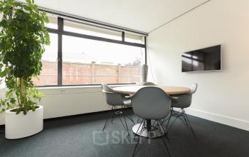 Vergaderruimte in Den Haag met ronde tafel en zes stoelen, grote ramen voor natuurlijk licht. Perfecte kantoorruimte huren voor bijeenkomsten.