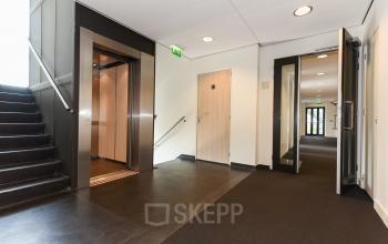 Een modern kantoorpand op Bezuidenhoutseweg 161 in Den Haag met een strak ingerichte gang die toegang biedt tot een lift en verschillende kantoren. Perfect voor kantoorruimte huren in Haagse Hout.