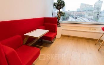 Moderne loungehoek met rode zitbank en uitzicht op de skyline van Den Haag Haagse Hout, ideaal voor een kantoorpand aan de Jan Pietersz. Coenstraat 7.