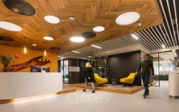Modern kantoorpand op Prinses Margrietplantsoen 25 in Den Haag Haagse Hout, met stijlvolle inrichting, opvallend houten plafond en opvallende verlichting. Personen zijn in gesprek bij de receptie, wat zakelijke activiteit suggereert.