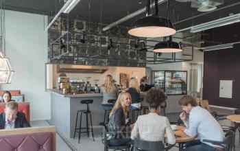 Moderne kantoorlounge met professionals die overleggen en ontspannen in kantorencomplex aan de Oude Middenweg 3-19, Den Haag.