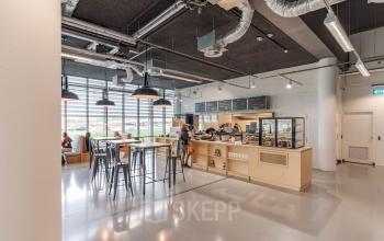 Moderne kantoorruimte met een pantry, hoge stoelen bij countertop en een persoon die koffie serveert in het pand aan Oude Middenweg 3-19 in Den Haag.