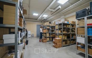 Een kantoorpand aan Tauber 52, Den Haag Leidschenveen-ypenburg, waarin een persoon dozen in stellingen plaatst voor opslag. Ruime en georganiseerde omgeving voor praktisch gebruik.