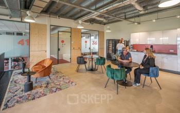 Moderne kantoorpandinterieur op Tauber 52 in Den Haag met een open werkruimte en kleurrijke meubelen, waar mensen zijn bezig met zakelijke gesprekken en samenwerken.