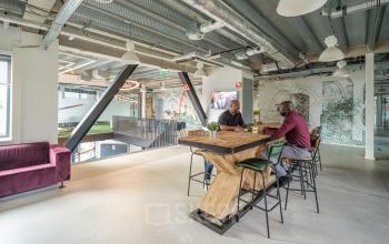 Moderne kantoorruimte huren in het kantoorpand op Tauber 52, Den Haag Leidschenveen-Ypenburg, met een open vloerplan en gemeubileerde zitplaatsen, waar mensen overleggen aan een houten tafel.