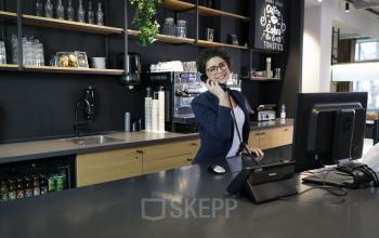 Kantoorruimte huren op President Kennedylaan 19 in Den Haag Statenkwartier. Een medewerker staat bij de receptie en voert zakelijke telefoongesprekken. De ruimte is modern ingericht met kasten en een werkstation.