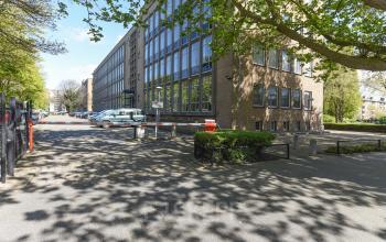 Exterieur van het kantoorpand aan de President Kennedylaan 19 in Den Haag Statenkwartier, met parkeerplaatsen en toegangsweg. Ideaal voor kantoorruimte huren in een groene omgeving nabij voorzieningen.