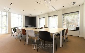 Vergaderruimte met lange tafels en diverse stoelen in een lichte kantoorruimte gelegen aan President Kennedylaan 19, Den Haag Statenkwartier, beschikbaar voor kantoorruimte huren.