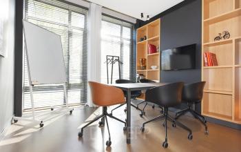 Moderne kantoorruimte in Den Haag met grote ramen, een tafel met vijf stoelen, een whiteboard en een open kast. Geschikt voor vergaderingen of brainstormsessies.
