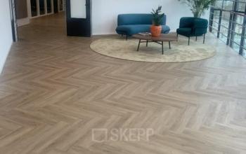 Moderne kantoorruimte met houten vloer, twee blauwe fauteuils en een kleine bank aan Johan de Wittlaan 3-7, Den Haag Statenkwartier. Ruimte biedt volop licht en uitzicht voor bedrijven die kantoorruimte huren.