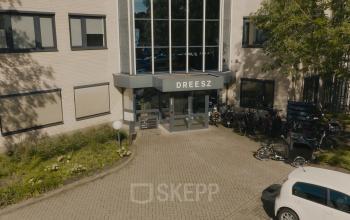 Exterieur van een kantoorpand aan de Keulenstraat 9 in Deventer, omgeven door fietsenrekken en groenvoorzieningen. Het gebouw heeft grote ramen en een moderne entree. Ideaal voor bedrijven die kantoorruimte willen huren.