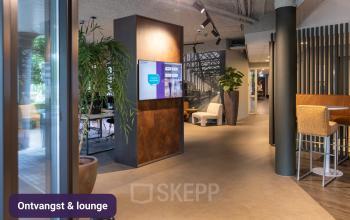 Ontvangst en loungegedeelte in een modern kantoorpand op Keulenstraat 12, Deventer, met comfortabel zitmeubilair en een digitale display. Ideaal voor wie op zoek is naar kantoorruimte huren.