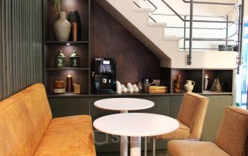 Gezellige werkruimte in het kantoorpand op Keulenstraat 12, Deventer, voorzien van comfortabele zitplaatsen, tafels, en een koffiezetapparaat onder een trap.