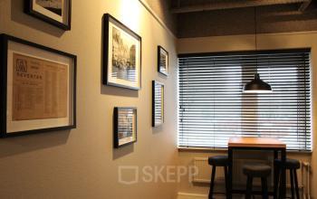Kantoorruimte in Deventer aan de Keulenstraat 12 met hoge zit aan een houten tafel, barkrukken, en wanddecoratie.