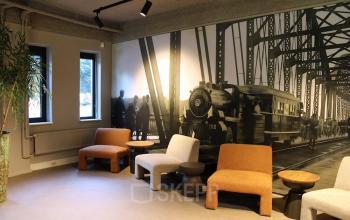 Gedeelde lounge-ruimte in het kantoorpand op Keulenstraat 12, Deventer, met comfortabele zitbanken en een wand met kunstwerk van een oude stoomtrein.