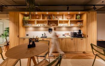 Stijlvolle kantoorruimte te huur op Diemerhof 42, Diemen, met moderne houten inrichting en een persoon bij de koffieautomaat. Ideaal voor vergaderingen en informeel overleg in een aantrekkelijke kantoorpand omgeving.