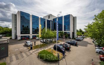 Het kantoorpand Diemermere 11-19 in Diemen met moderne glazen gevel en ruime parkeerplaats voor het gebouw.