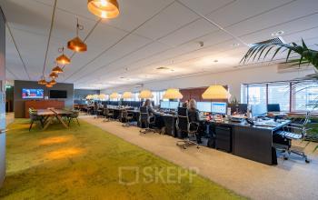Moderne kantoorruimte in Dordrecht met open werkruimte, groene vloerbedekking en plafondverlichting. Mensen werken geconcentreerd aan bureaus met computers, wat een professionele sfeer creëert.