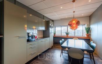 Kantoorruimte huren op Mijlweg 61 in Dordrecht met moderne keuken, vergadertafel en stoelen. Heldere verlichting en decoratieve planten creëren een uitnodigende sfeer.