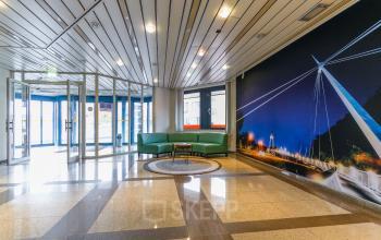 Ingangsruimte van kantoorpand op Van Knobelsdorffplein 14 in Drachten. De ruimte heeft een moderne uitstraling met glazen deuren en een comfortabele groene bank.