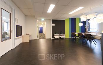 Moderne kantoorruimte huren aan Van Knobelsdorffplein 14, Drachten, met strakke inrichting, kleurrijke muren, en grote tafel met stoelen. Heldere verlichting en functioneel ontwerp maken het geschikt voor zakelijk gebruik.