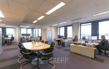 Kantoor op Van Knobelsdorffplein 14 in Drachten met ruim opgezette werkplekken en vergadertafel. Drie mensen zijn bezig met computerwerkzaamheden. Kantoorruimte huren hier biedt een lichte, functionele werkomgeving.