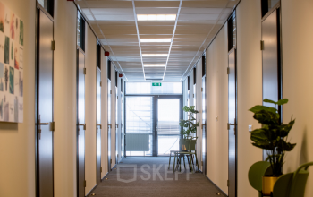 Kantoorpand aan de Galvanistraat 7 in Ede met lange gang, witte muren en planten. Geschikt voor kantoorruimte huren, met verschillende deuren aan beide zijden van de gang.
