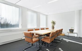 Lichte en ruime vergaderruimte met een houten tafel en comfortabele stoelen in een kantoorpand aan de Celsiusstraat 34, Ede. Perfect voor wie kantoorruimte huren wil. Grote ramen bieden veel natuurlijk licht.