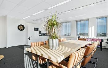 Ruime kantoorruimte met grote ramen op Celsiusstraat 34 in Ede, voorzien van een lange houten tafel met stoelen en een grote plant voor een moderne uitstraling. Ideaal voor kantoorruimte huren.