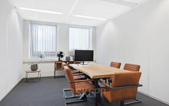 Kantoorruimte huren in een licht kantoor op Celsiusstraat 34, Ede, met een houten tafel, vier bruine stoelen en een monitor.