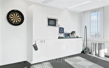 Lichte kantine met witte kasten en een dartbord, ideaal voor een ontspannende pauze tijdens het kantoorruimte huren in Ede.