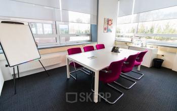 Vergaderruimte met groot raam, witte tafel en roze stoelen in kantoor Flight Forum 40 Eindhoven Airport.