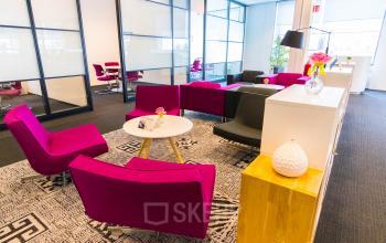 Grote, kleurrijke lounge met moderne meubels in kantoorpand Flight Forum 40, Eindhoven Airport. Knusse zitplekken met paarse stoelen en witte tafels bieden een gastvrije indruk voor wie kantoorruimte wil huren.