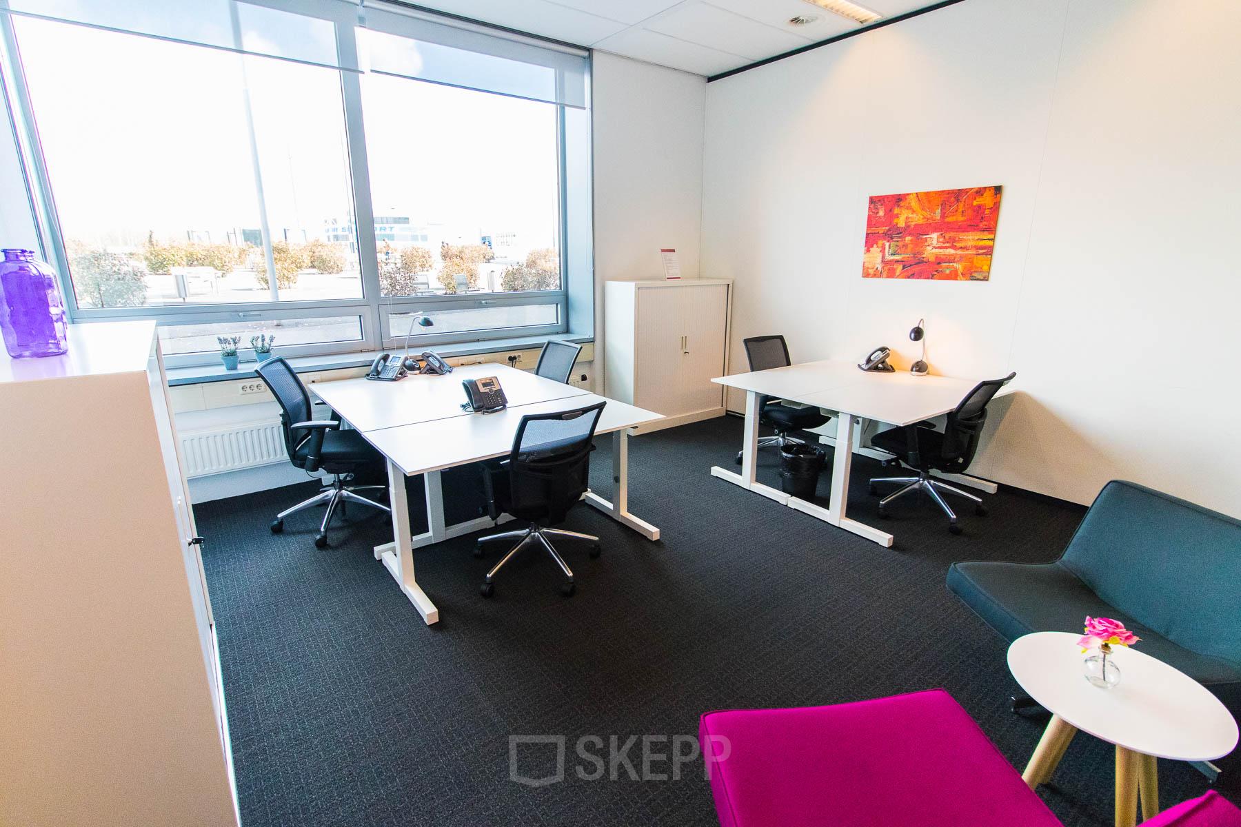 Moderne kantoorruimte huren op Flight Forum 40 in Eindhoven Airport met drie bureaus, stoelen en kleurrijke decoratie bij het raam.
