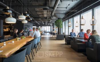 Moderne, gezellige kantoorruimte op Flight Forum 760-780 in Eindhoven Airport met grote tafels en mensen in overleg en aan het werk.