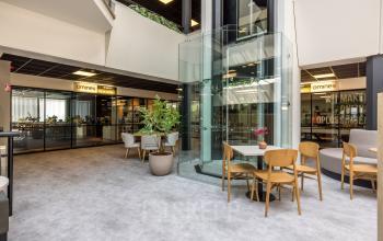 Moderne kantoorruimte huren in Eindhoven Airport met glazen lift en zitgedeelte rondom, ideaal voor flexwerken.