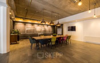 Stijlvolle vergaderzaal met lange houten tafel en gekleurde stoelen, ideaal voor kantoorruimte huren op Eindhoven Airport.