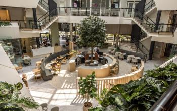 Moderne en open ingerichte lounge in een kantoorpand met veel groen en zitgelegenheid. Huur hier je kantoorruimte en geniet van een inspirerende omgeving aan de Luchthavenweg 81 in Eindhoven Airport.