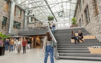 Moderne kantoorruimte met glazen dak op Flight Forum 120-159 in Eindhoven Airport, waar mensen werken en socializen op verschillende niveaus. Ideaal om kantoorruimte te huren in een inspirerende omgeving.