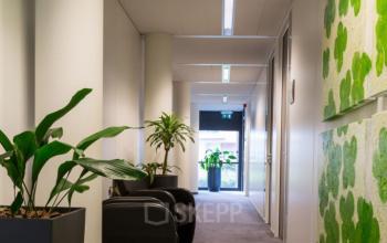 Kantoorpand aan Luchthavenweg 55, Eindhoven Airport, met moderne gang voorzien van kunstwerken en planten, ruimte om kantoorruimte te huren.